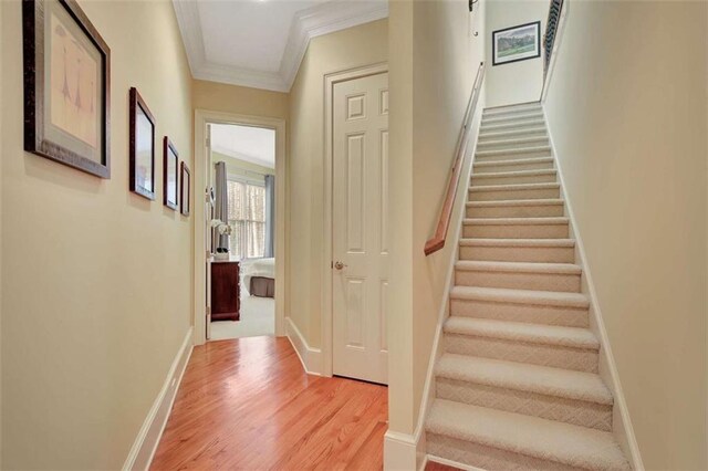 stairway with ornamental molding, wood finished floors, and baseboards