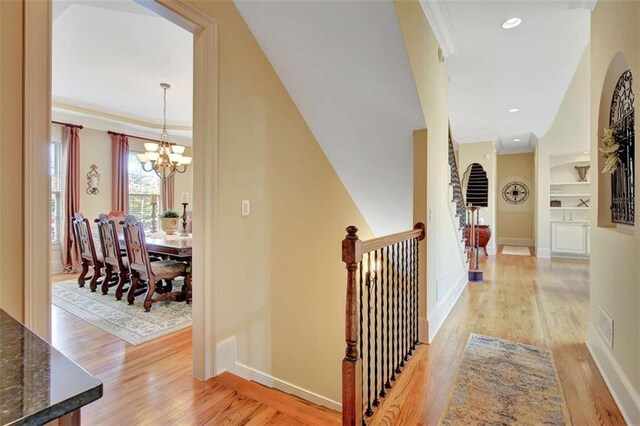 corridor with light wood-style floors, a chandelier, crown molding, baseboards, and built in features