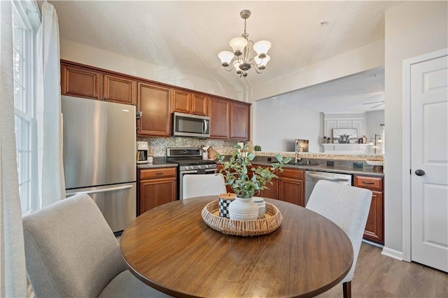 kitchen featuring stainless steel appliances, a chandelier, wood finished floors, tasteful backsplash, and brown cabinets