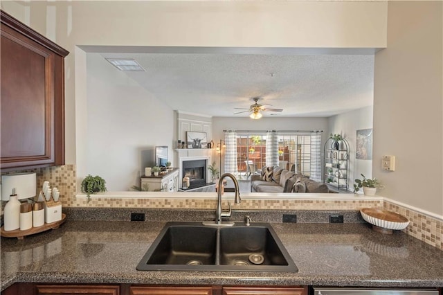 kitchen with a sink, a fireplace, open floor plan, tasteful backsplash, and a ceiling fan