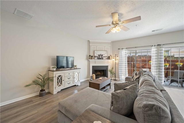 living area featuring wood finished floors, a ceiling fan, a textured ceiling, baseboards, and a large fireplace