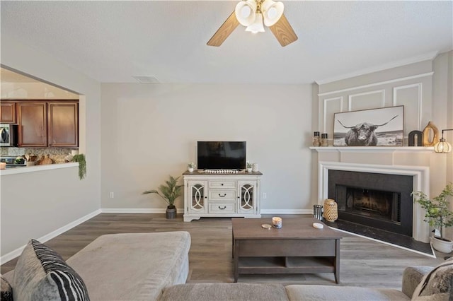 living area with ceiling fan, wood finished floors, a fireplace with raised hearth, a textured ceiling, and baseboards