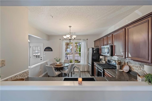 kitchen featuring appliances with stainless steel finishes, a sink, a chandelier, a textured ceiling, and backsplash
