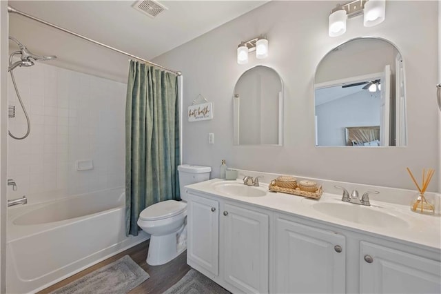full bath featuring toilet, shower / tub combo with curtain, double vanity, wood finished floors, and a ceiling fan