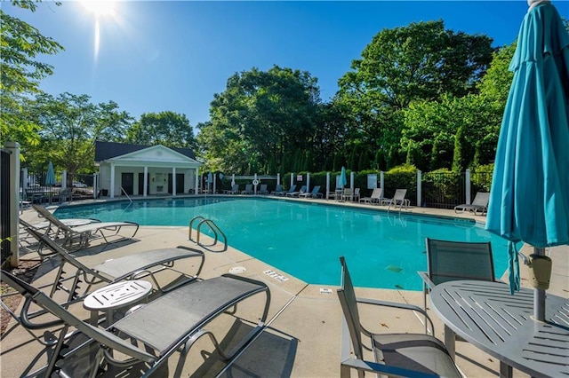 community pool with fence, a patio area, and view of wooded area