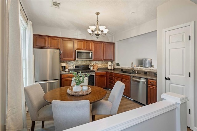 kitchen with stainless steel appliances, a sink, a chandelier, tasteful backsplash, and brown cabinets