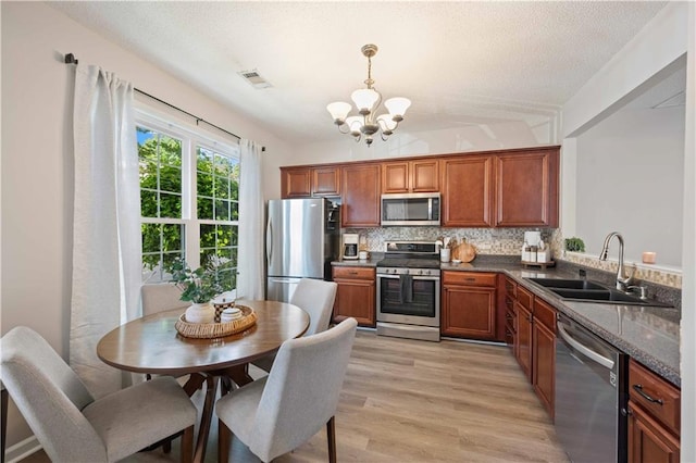 kitchen with stainless steel appliances, a sink, a chandelier, decorative backsplash, and brown cabinets