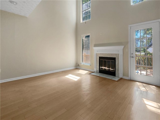 unfurnished living room featuring a high end fireplace, a textured ceiling, a towering ceiling, and light hardwood / wood-style floors