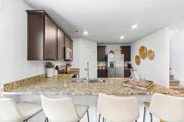 kitchen featuring dark brown cabinets, sink, light stone countertops, and stainless steel appliances