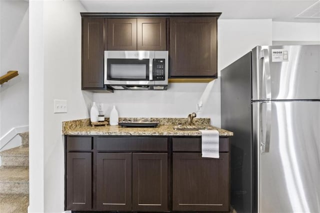 kitchen featuring dark brown cabinetry, light stone counters, sink, and appliances with stainless steel finishes