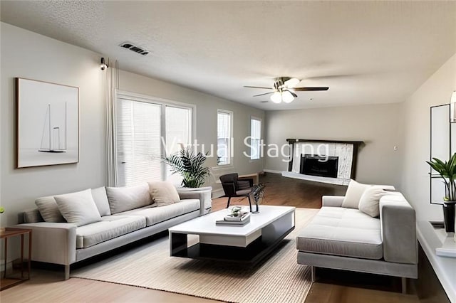 living area with a fireplace with raised hearth, wood finished floors, visible vents, and ceiling fan