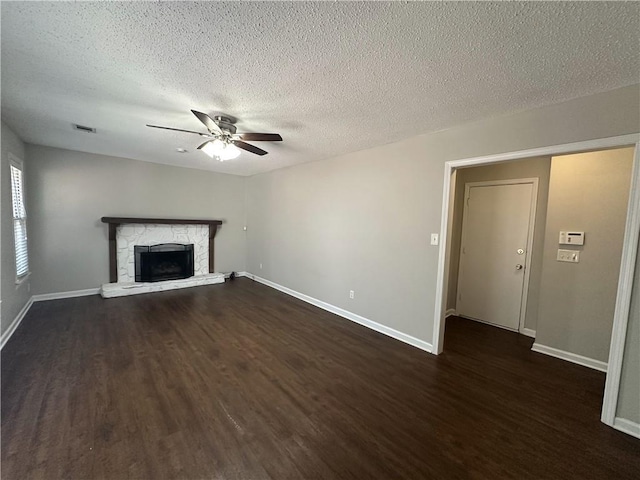 unfurnished living room with a ceiling fan, a textured ceiling, a stone fireplace, baseboards, and dark wood-style flooring