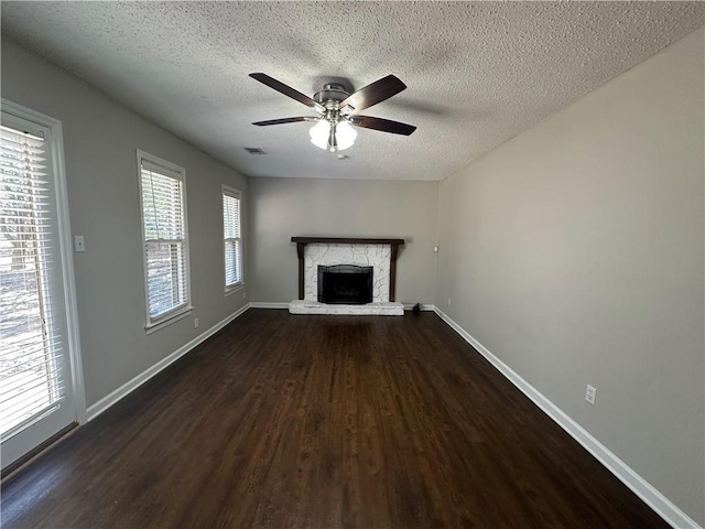 unfurnished living room with visible vents, baseboards, a stone fireplace, a ceiling fan, and dark wood-style flooring