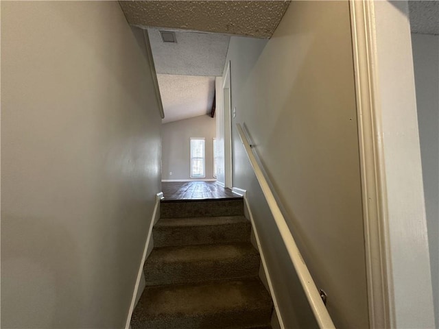 stairs with visible vents, a textured ceiling, carpet floors, baseboards, and vaulted ceiling