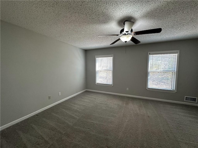 spare room with a ceiling fan, visible vents, dark carpet, and baseboards