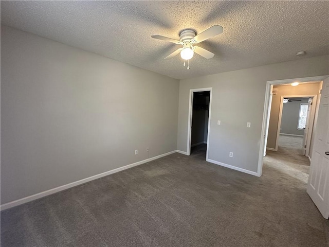 unfurnished bedroom featuring a ceiling fan, baseboards, a textured ceiling, a walk in closet, and dark carpet