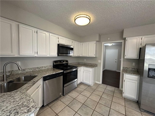 kitchen with a sink, stainless steel appliances, light stone counters, and white cabinetry