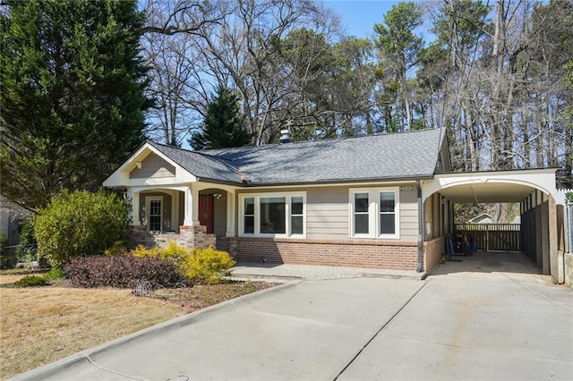 view of front of property featuring a carport, fence, roof with shingles, concrete driveway, and brick siding