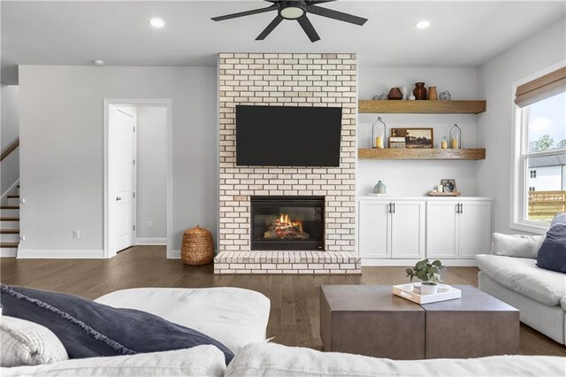 living room with ceiling fan, dark wood-type flooring, and a brick fireplace