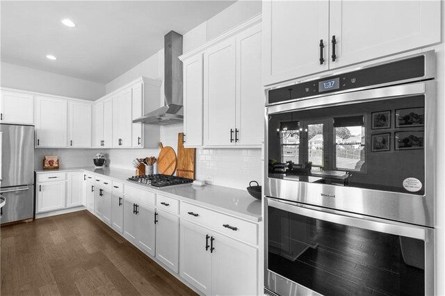 kitchen with wall chimney range hood, appliances with stainless steel finishes, dark hardwood / wood-style floors, and white cabinets