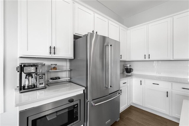 kitchen with appliances with stainless steel finishes, white cabinetry, backsplash, and dark hardwood / wood-style floors