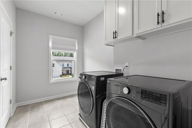 laundry room with light tile patterned flooring, cabinets, and washer and clothes dryer