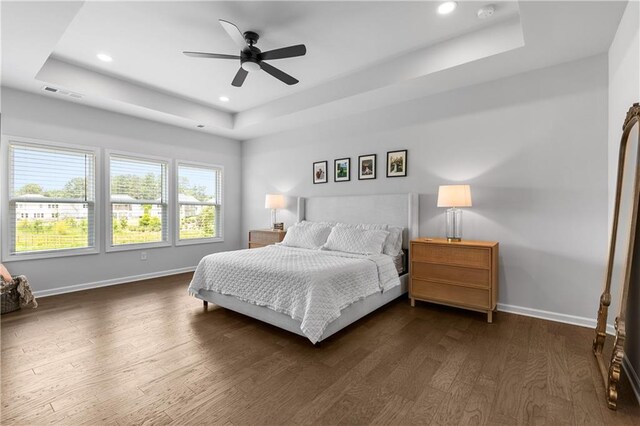 bedroom with dark wood-type flooring, ceiling fan, and a raised ceiling