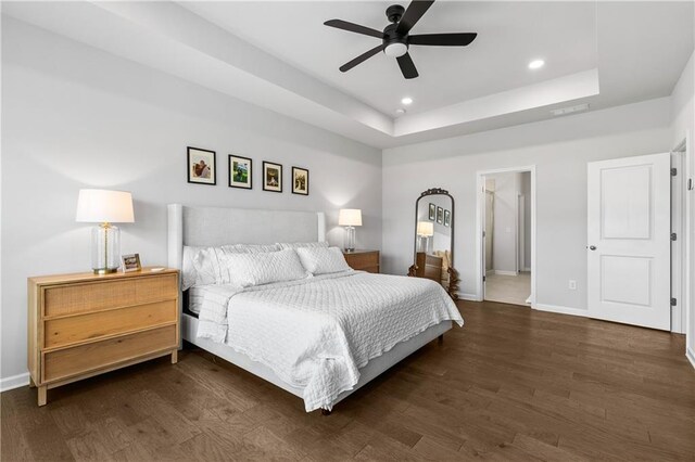 bedroom with ceiling fan, a raised ceiling, ensuite bathroom, and dark hardwood / wood-style floors