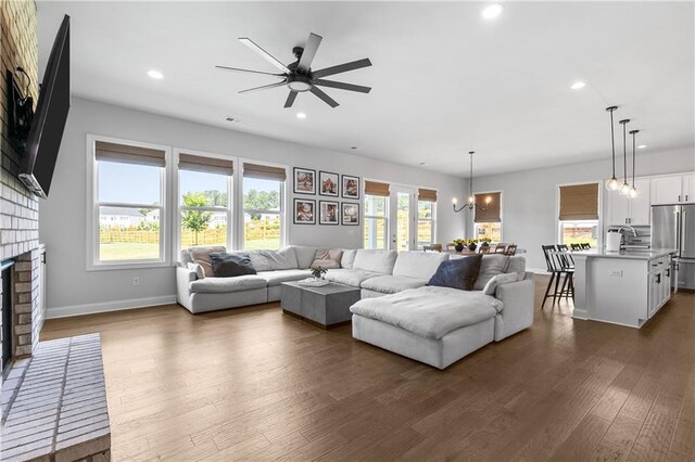 living room featuring ceiling fan with notable chandelier, a fireplace, dark hardwood / wood-style floors, and a healthy amount of sunlight