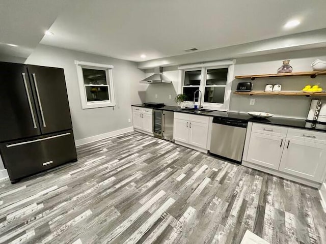 kitchen with dishwasher, light wood-type flooring, black refrigerator, wall chimney range hood, and sink