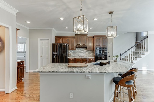 kitchen featuring a large island with sink, decorative light fixtures, a breakfast bar area, and black appliances