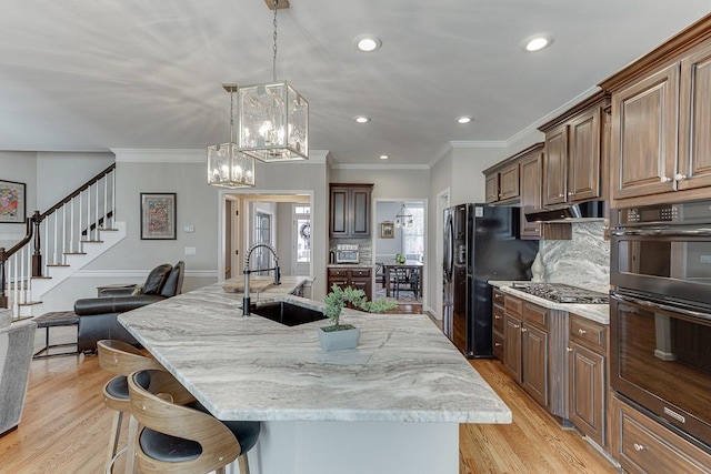 kitchen with a breakfast bar, black appliances, hanging light fixtures, sink, and a large island