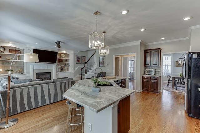 kitchen featuring light stone counters, a kitchen bar, a kitchen island with sink, black refrigerator, and light wood-type flooring