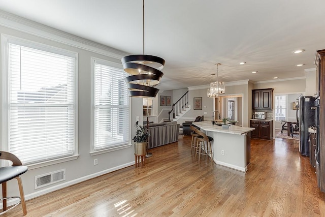 kitchen with dark brown cabinetry, pendant lighting, a chandelier, a breakfast bar area, and an island with sink