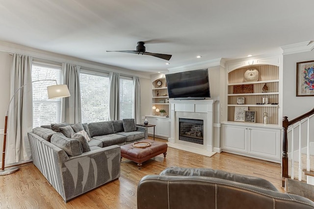 living room with built in shelves, light hardwood / wood-style flooring, ceiling fan, and crown molding