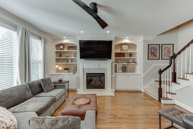 living room featuring light hardwood / wood-style floors, built in features, ceiling fan, and ornamental molding