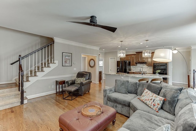 living room featuring sink, light hardwood / wood-style flooring, ceiling fan with notable chandelier, and ornamental molding