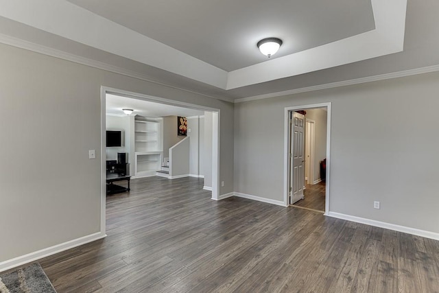 spare room with built in shelves, a raised ceiling, and dark wood-type flooring