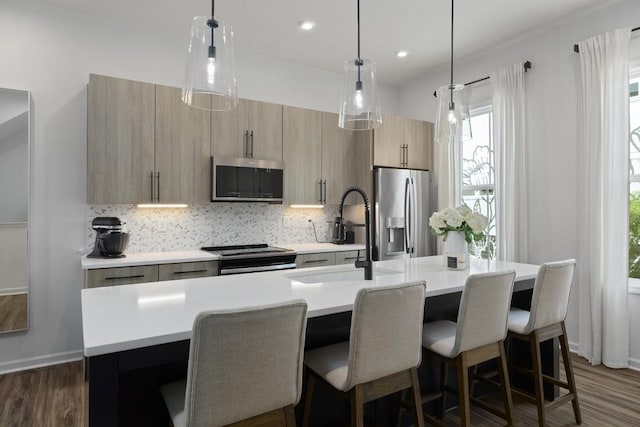 kitchen with stainless steel appliances, decorative light fixtures, and an island with sink