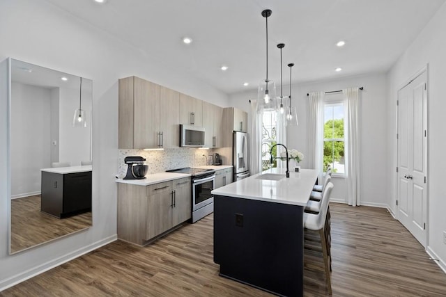 kitchen featuring light brown cabinetry, appliances with stainless steel finishes, sink, pendant lighting, and a center island with sink