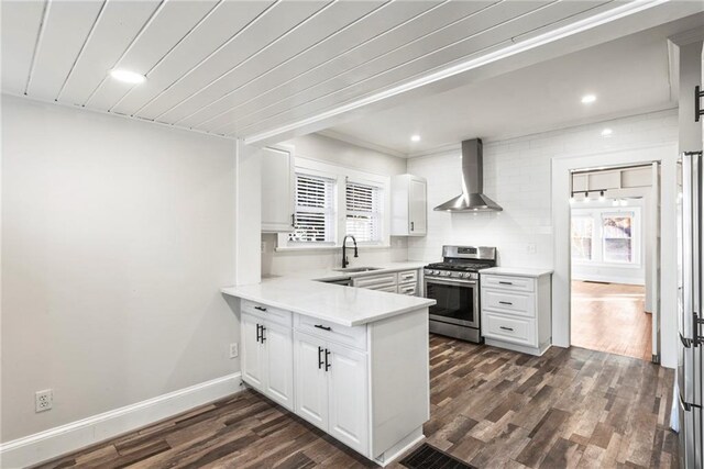 kitchen featuring stainless steel gas range oven, wall chimney exhaust hood, dark wood-type flooring, sink, and white cabinets