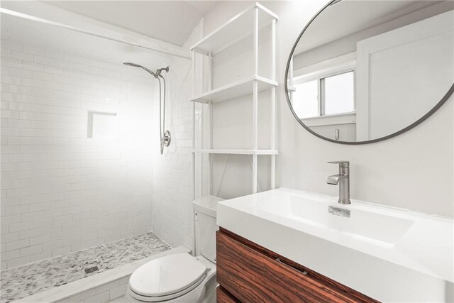 bathroom featuring a tile shower, vanity, and toilet