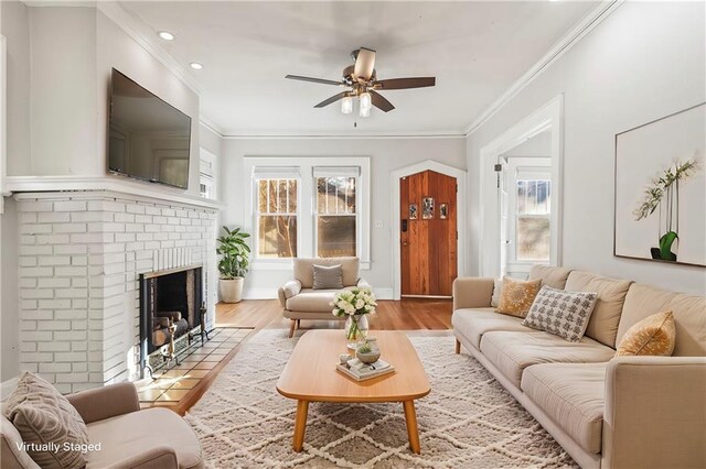 living room with ceiling fan, crown molding, light hardwood / wood-style flooring, and a brick fireplace