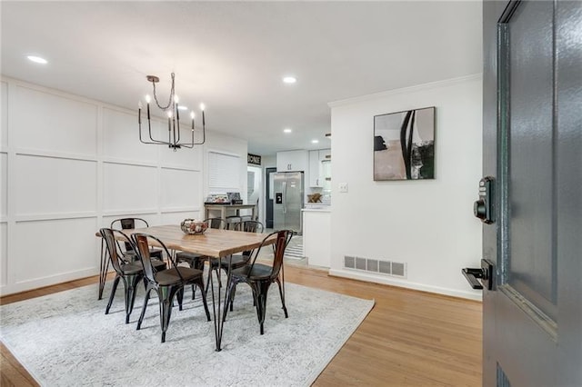 dining space with light wood-type flooring, crown molding, and a chandelier