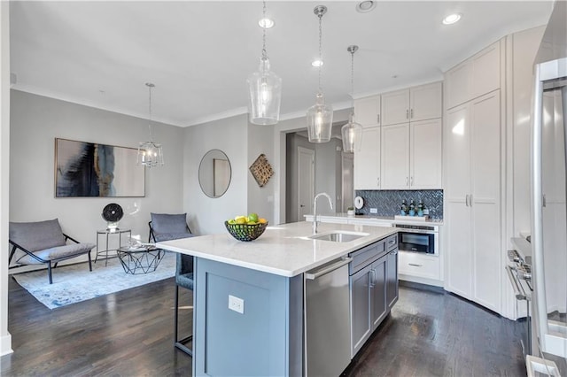 kitchen with sink, white cabinetry, hanging light fixtures, appliances with stainless steel finishes, and a kitchen island with sink