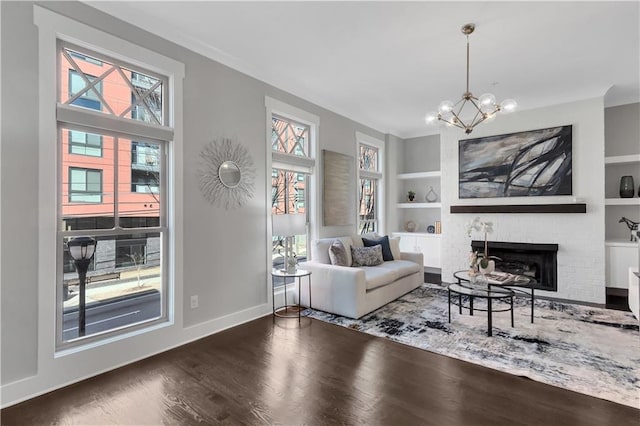 living room featuring hardwood / wood-style flooring, a brick fireplace, a notable chandelier, and built in shelves