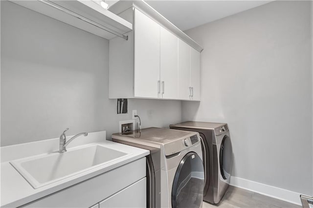 clothes washing area with sink, washing machine and dryer, cabinets, and light wood-type flooring