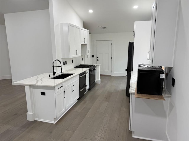 kitchen with white cabinets, light stone counters, wood finished floors, a sink, and gas stove