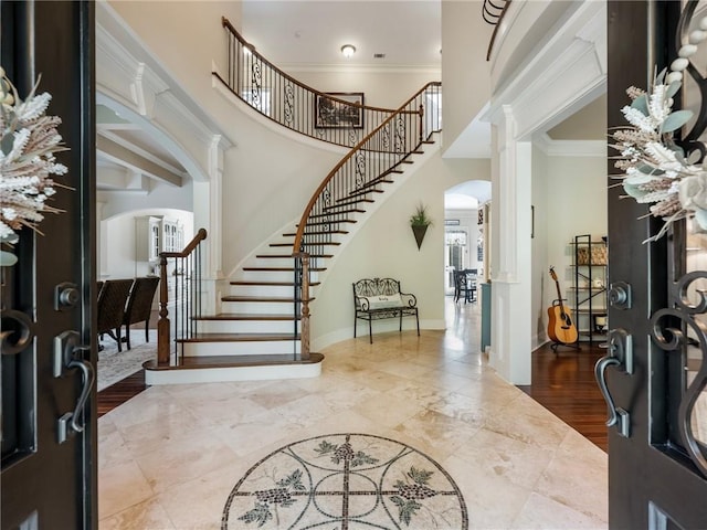 foyer entrance with crown molding, decorative columns, and a towering ceiling