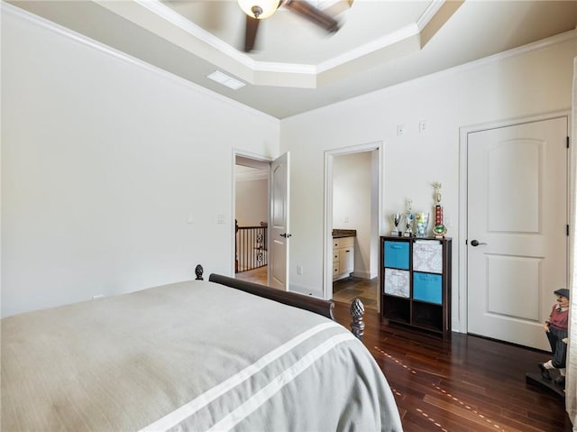 bedroom with crown molding, dark wood-type flooring, ensuite bath, ceiling fan, and a tray ceiling